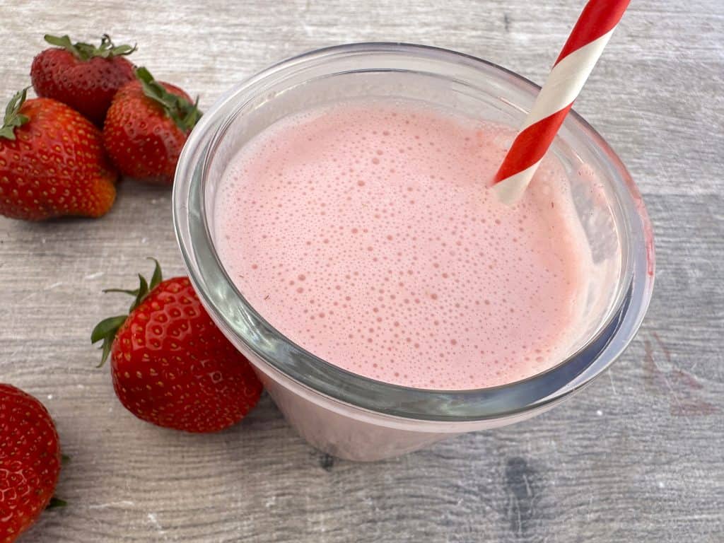 Strawberry lassi in glass with straw and strawberries nearby